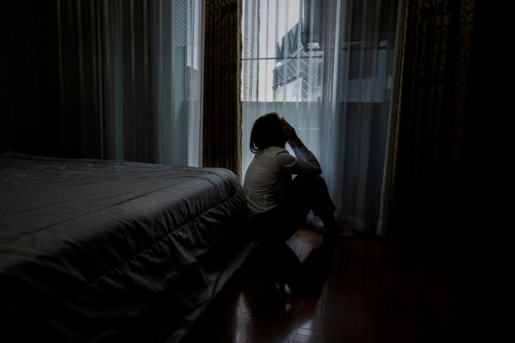 person sitting on floor in dark room while experiencing trauma and depression