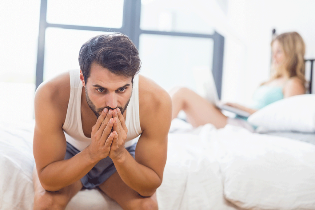 couple facing away from each other in bed while one exhibits signs of sex addiction