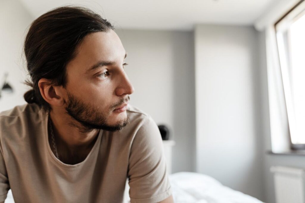 person sitting on bed with faraway look on face while struggling with the abuse of painkillers and alcohol