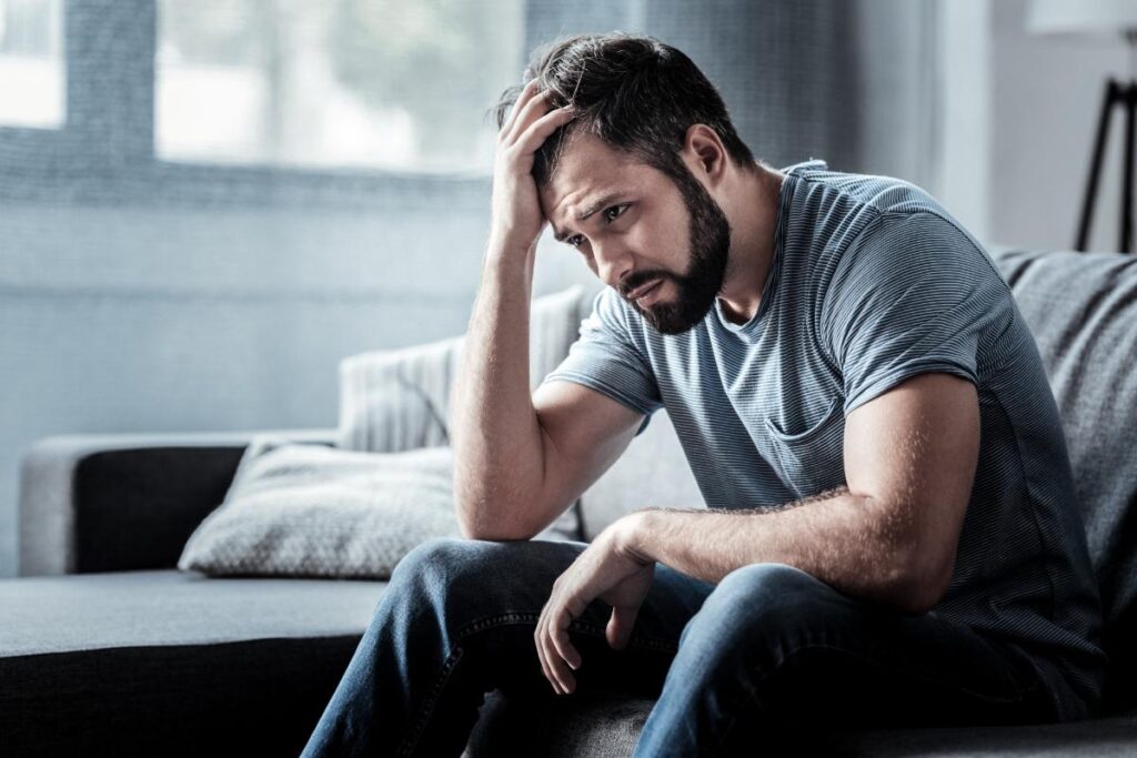 person sitting on edge of bed hanging head while wondering what to do after a relapse