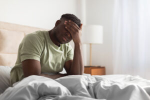 person in bed with hand over face experiencing chronic depression