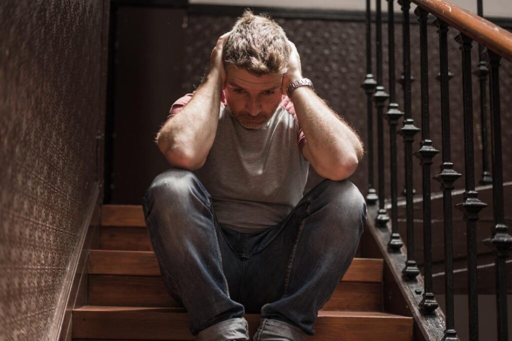 man sitting on steps with head in heads while experiencing signs of bipolar disorder in men